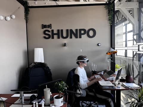 Un membre de l'équipe SHUNPO à son bureau, un casque de réalité virtuelle sur la tête, devant le logo SHUNPO.