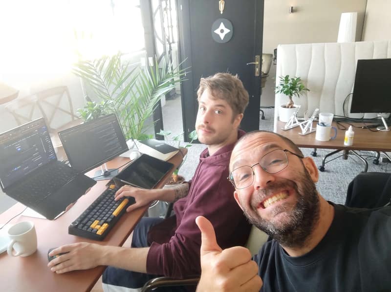 Deux membres de l'équipe SHUNPO à leurs bureaux, l'un d'eux faisant un pouce en l'air.