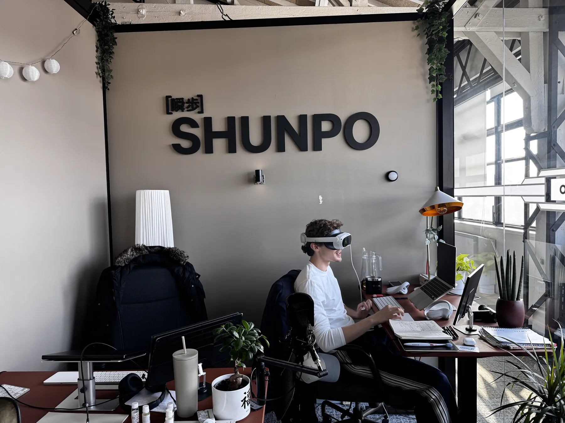 Un membre de l'équipe SHUNPO à son bureau, un casque de réalité virtuelle sur la tête, devant le logo SHUNPO.